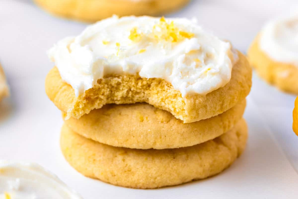 Lemon Sugar Cookies Two stacked sugar cookies with white frosting and lemon zest on top, the top cookie has a bite taken out of it.
