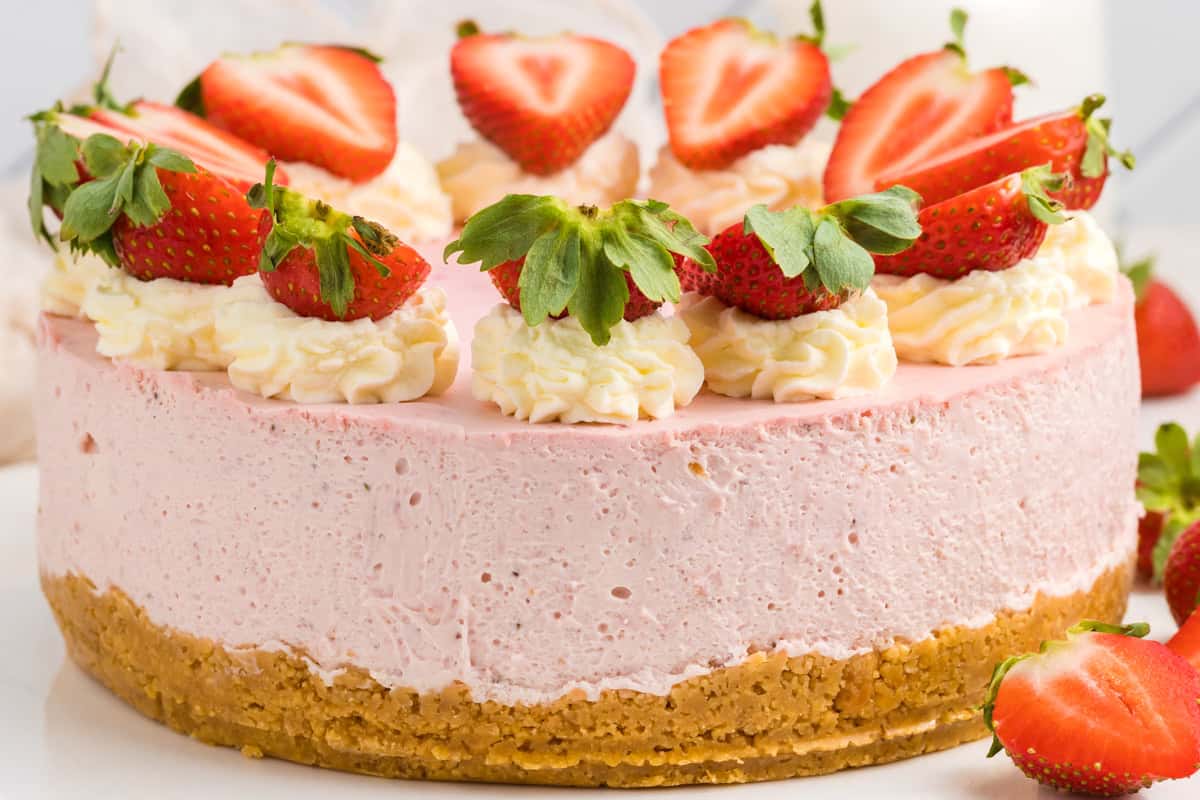 A strawberry cheesecake with a crumbly crust, topped with whipped cream swirls and fresh halved strawberries.