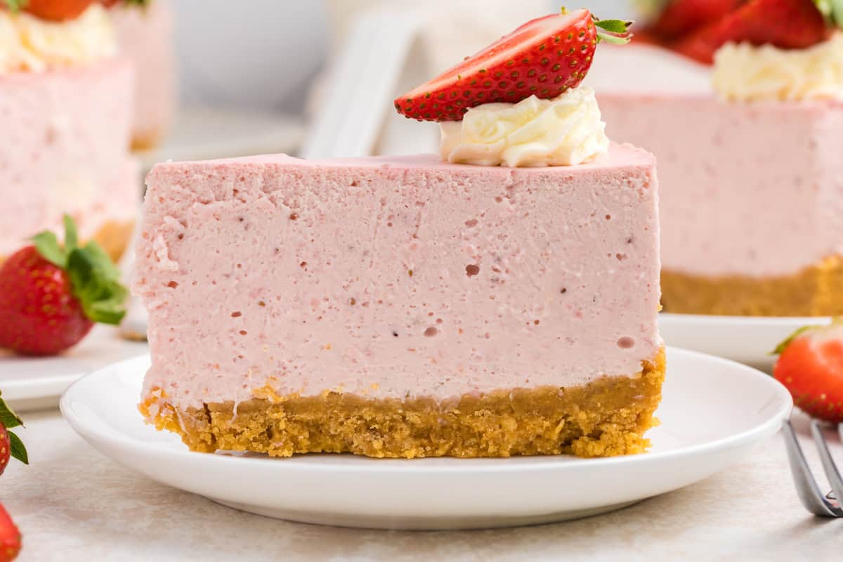 A slice of strawberry cheesecake with a crumbly graham cracker crust, topped with whipped cream and a halved strawberry.