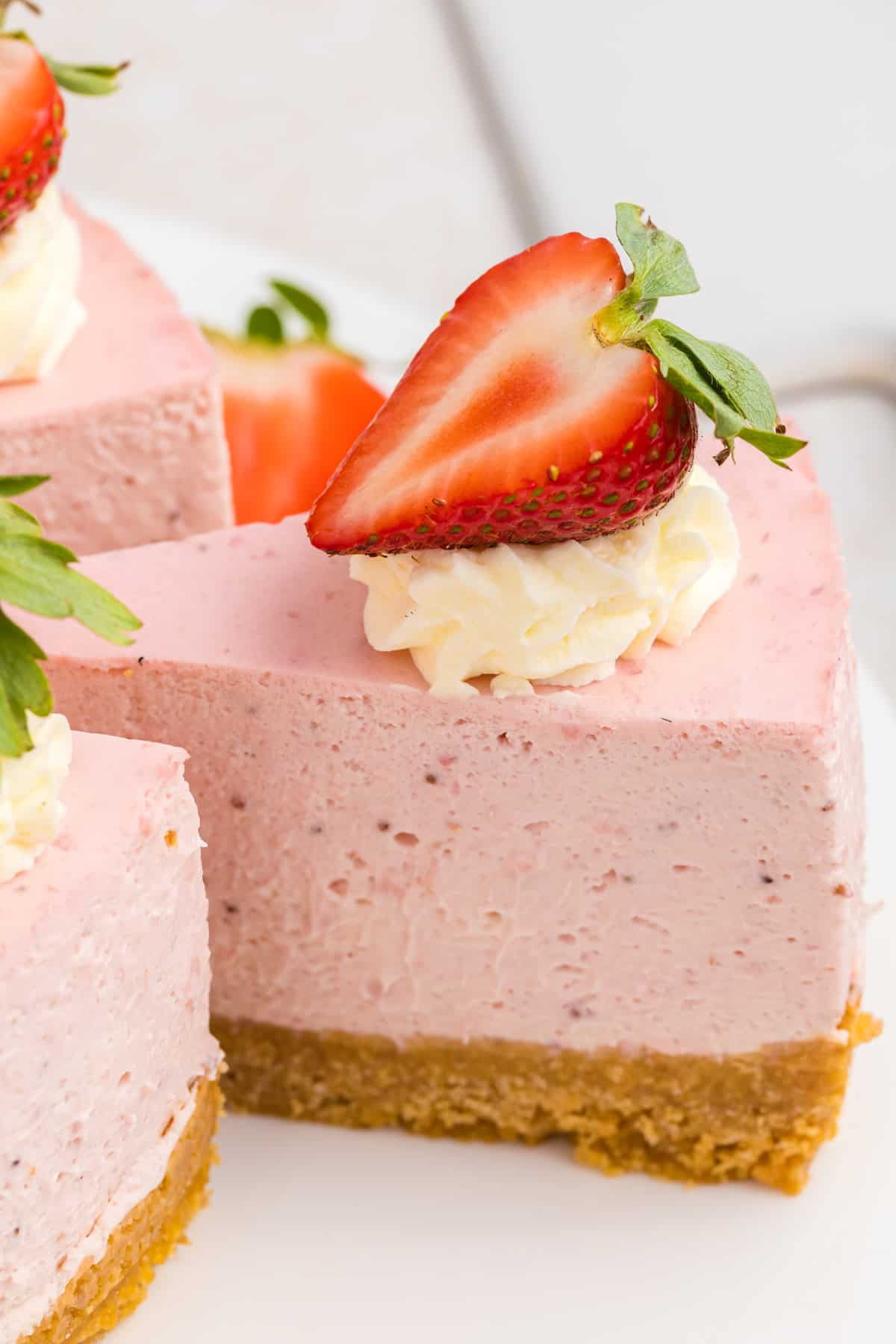 A slice of strawberry cheesecake with a graham cracker crust, topped with whipped cream and a halved fresh strawberry.