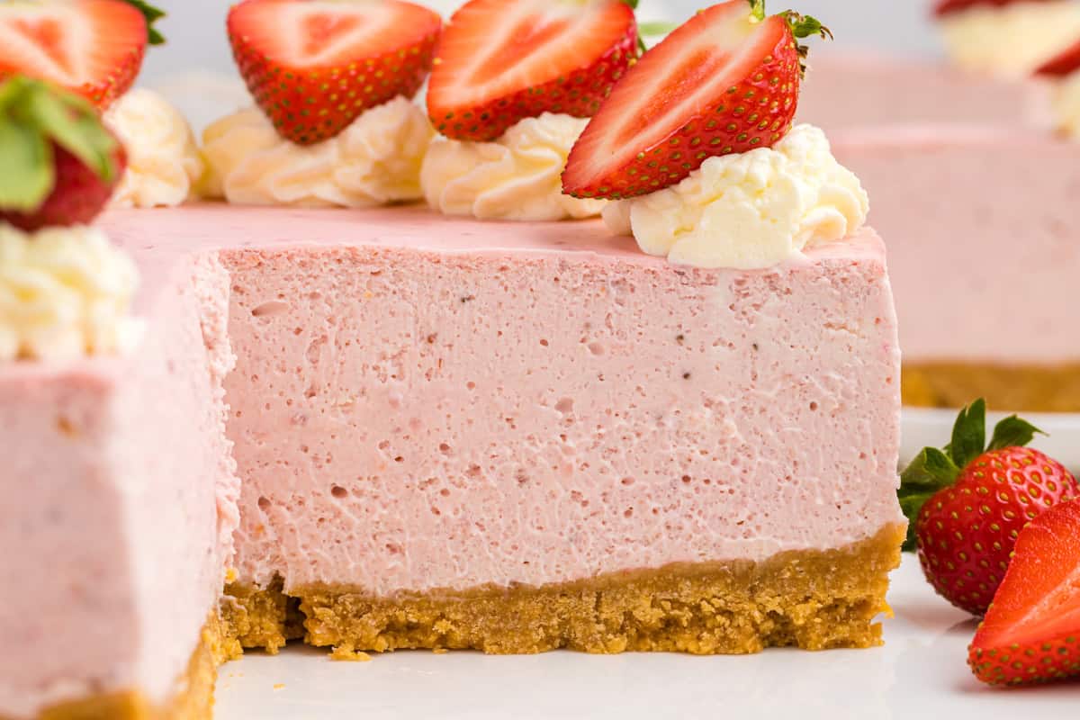 A close-up of a strawberry cheesecake with a graham cracker crust, topped with whipped cream and fresh strawberry halves.