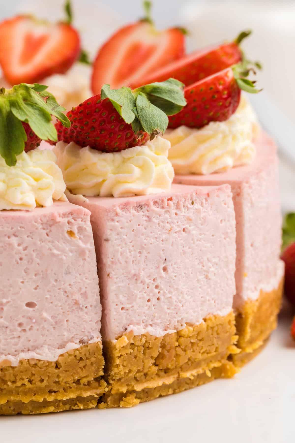 A close-up of a strawberry cheesecake with a graham cracker crust, topped with whipped cream and fresh halved strawberries.
