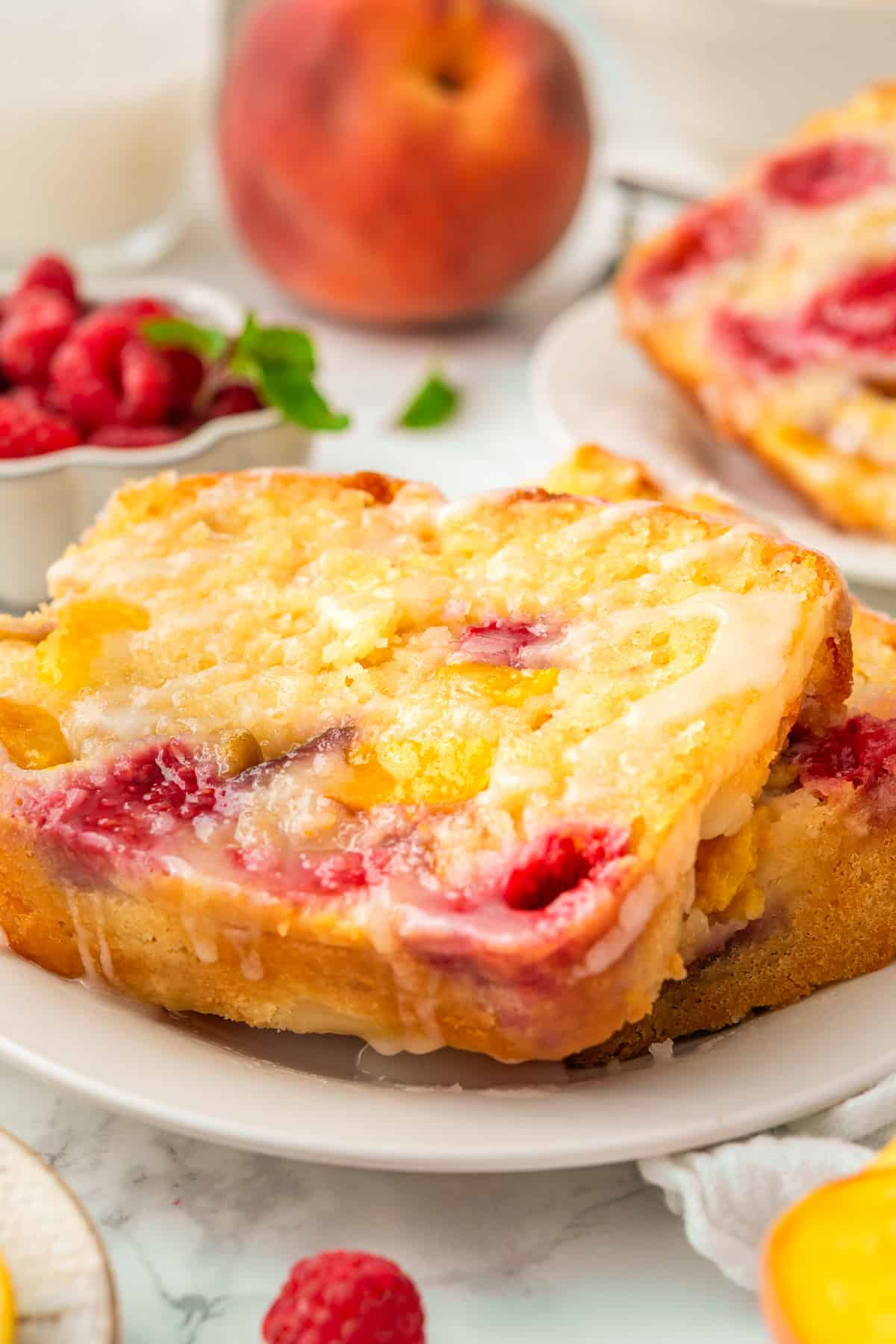 Raspberry Peach Loaf with Lemon Glaze A close-up of two slices of peach raspberry bread, topped with glaze, on a white plate.