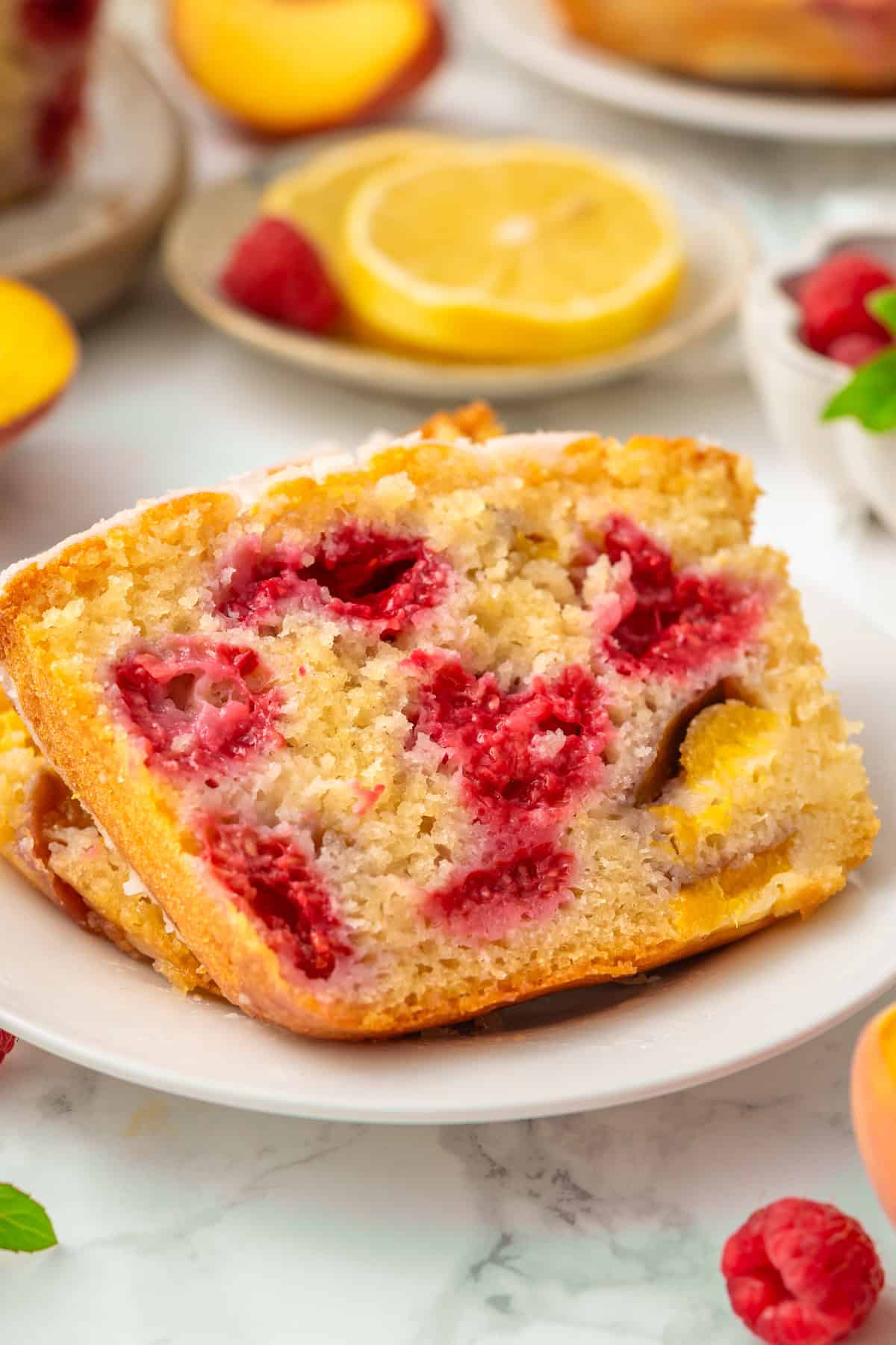 Raspberry Peach Loaf with Lemon Glaze Two slices of raspberry and peach loaf cake on a white plate, with visible fruit pieces.