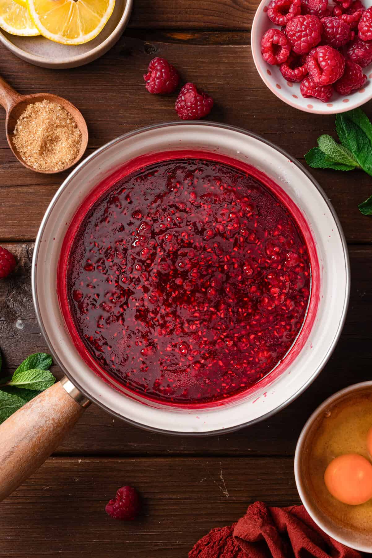 A saucepan of raspberry sauce sits on a wooden table.