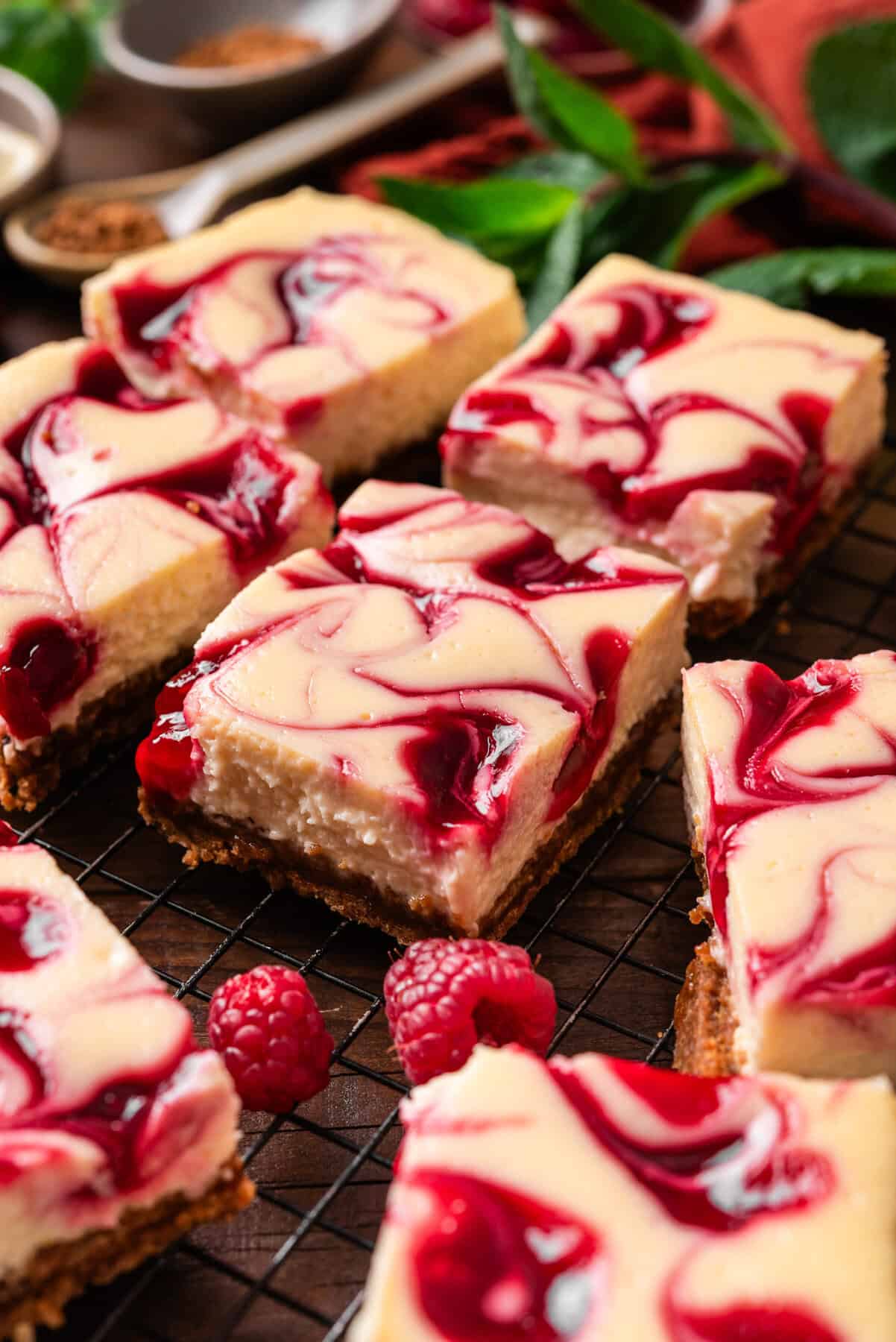Raspberry swirl cheesecake bars on a cooling rack. The bars have a creamy texture with vibrant raspberry swirls on top.