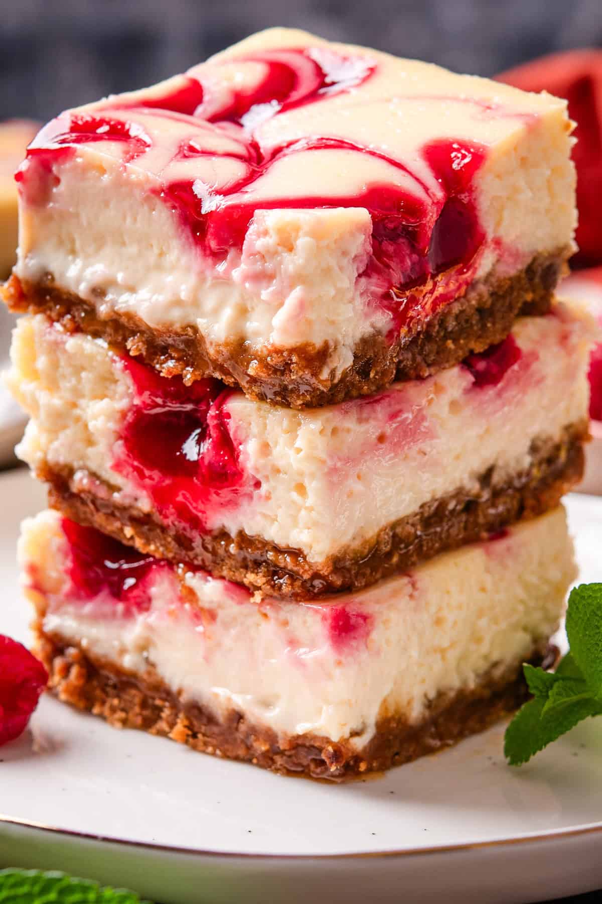 Three cheesecake bars with a golden crust and raspberry swirl on top are stacked on a plate. 
