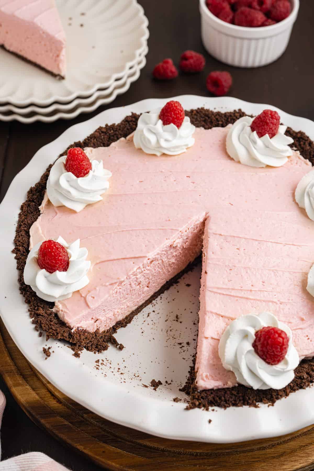 A pink raspberry cream pie with a chocolate crust, topped with whipped cream and fresh raspberries. 