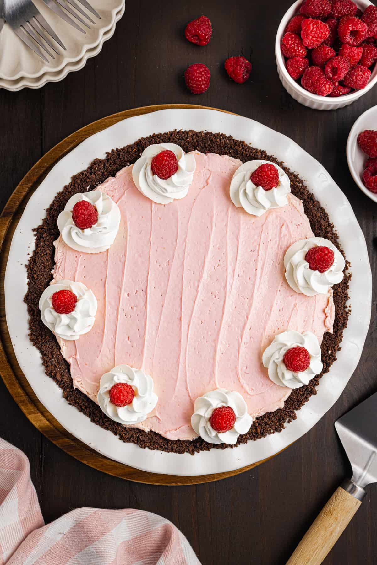 A raspberry cream pie with a chocolate crust, topped with swirls of whipped cream and fresh raspberries.