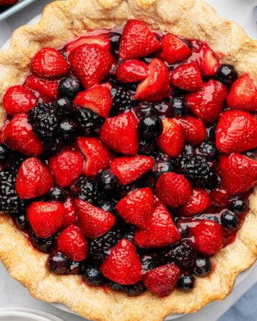 A baked pie crust filled with glossy fresh strawberries, blueberries, and blackberries arranged on top.