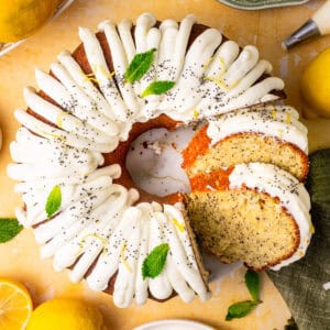 Lemon poppy seed bundt cake with white icing, lemon zest, poppy seeds, and mint leaves on top.