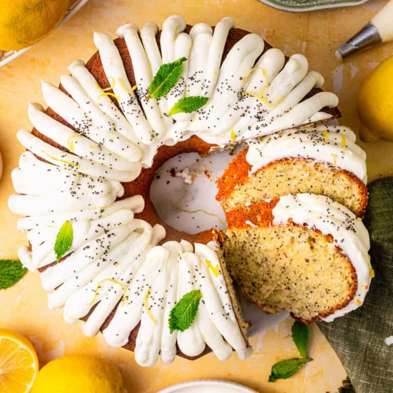 Lemon poppy seed bundt cake with white icing, lemon zest, poppy seeds, and mint leaves on top.
