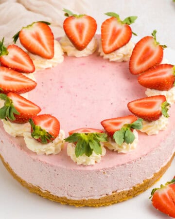 A pink strawberry cheesecake topped with whipped cream and halved fresh strawberries arranged in a circle.