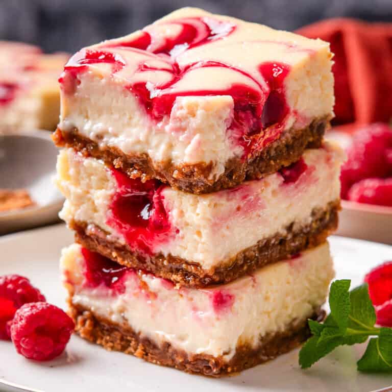 Three cheesecake bars with a graham cracker crust and raspberry swirl are stacked on a white plate.