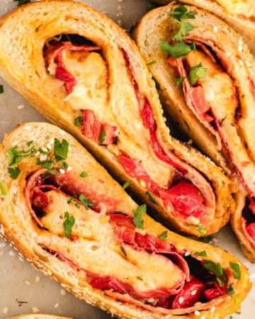 Sliced stromboli filled with melted cheese and pepperoni, garnished with chopped parsley and sesame seeds.