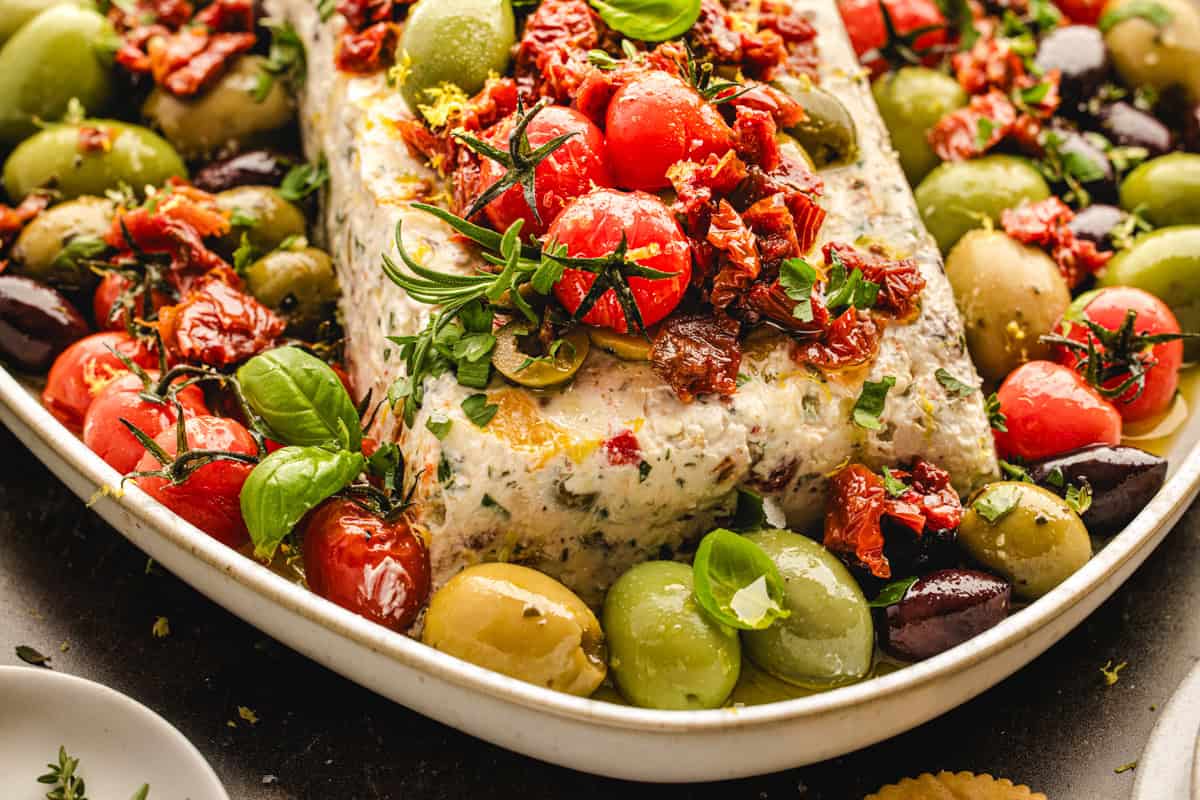 A rectangular herbed cheese log topped with cherry tomatoes and sun-dried tomatoes.
