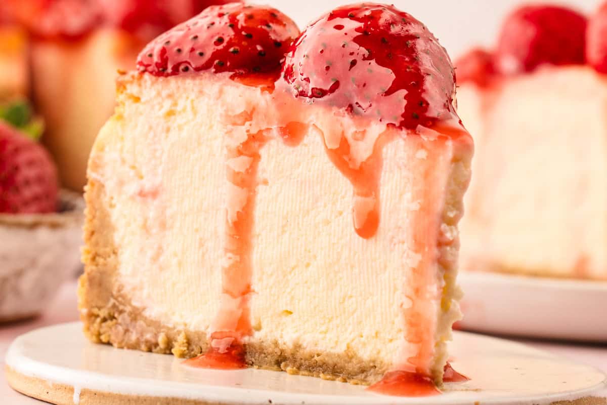 Classic New York-Style Cheesecake A slice of creamy cheesecake topped with glazed strawberries and strawberry sauce.