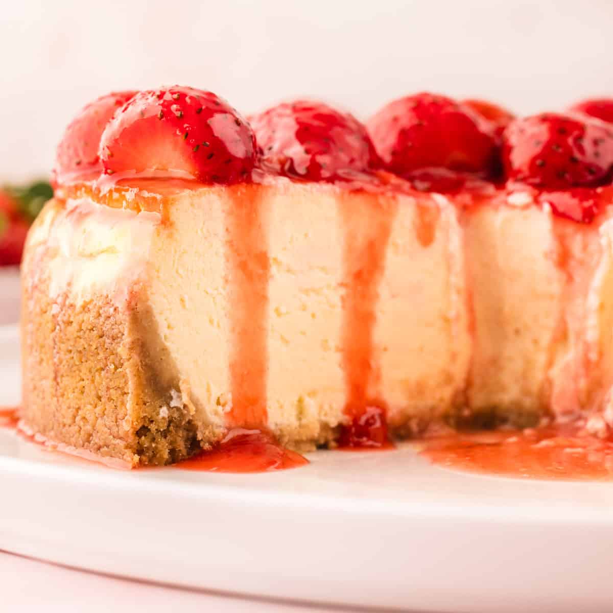 Classic New York-Style Cheesecake Close-up of a cheesecake topped with glazed strawberries and strawberry sauce, with a slice missing.