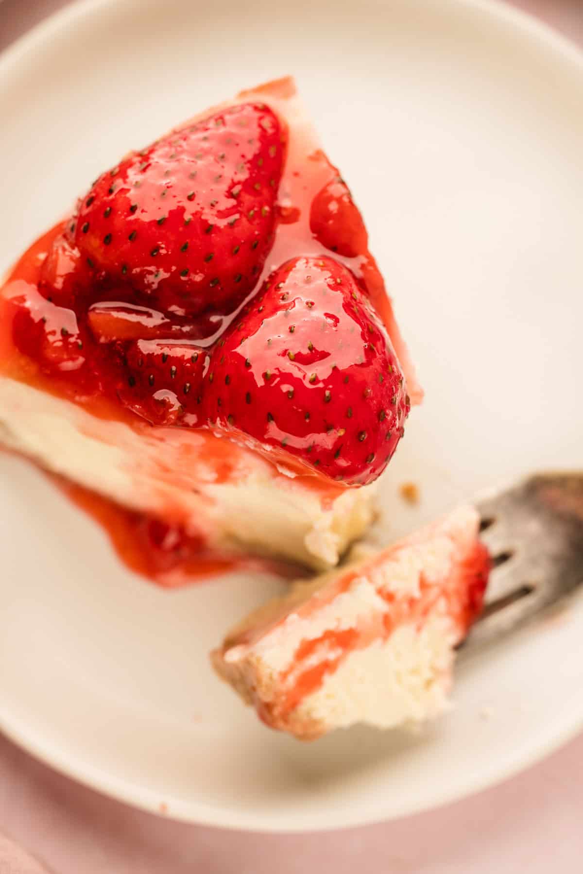 Classic New York-Style Cheesecake A slice of cheesecake topped with glazed strawberries on a white plate, with a fork holding a small bite.