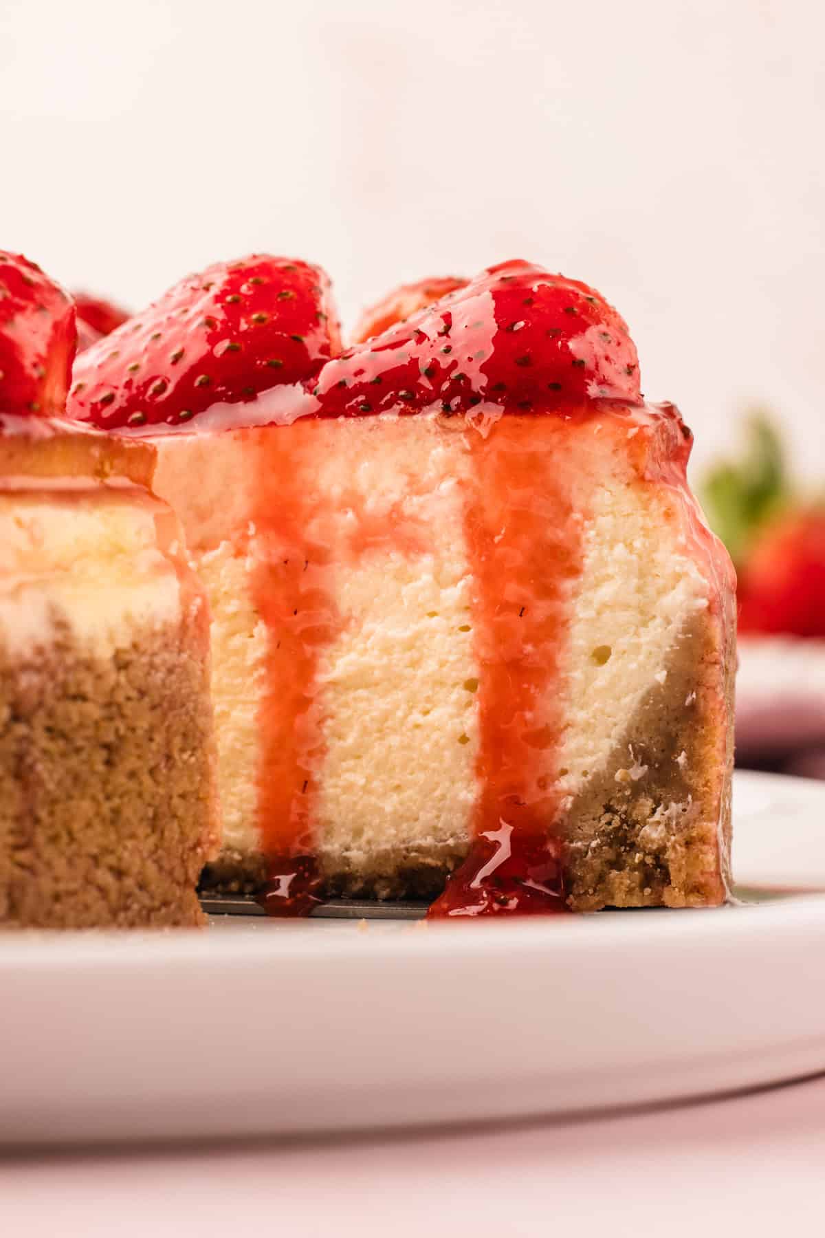 Classic New York-Style Cheesecake A close-up of a slice of cheesecake topped with glazed strawberries and strawberry sauce.