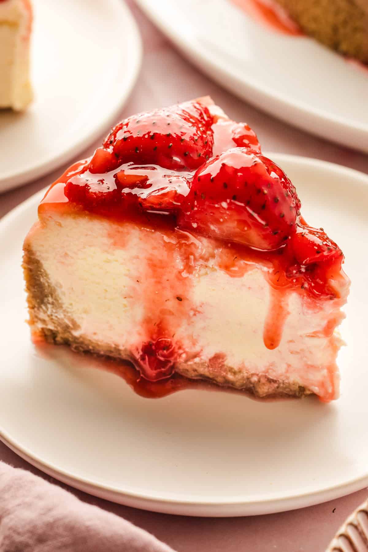 Classic New York-Style Cheesecake A slice of creamy cheesecake topped with glazed strawberries and strawberry sauce.