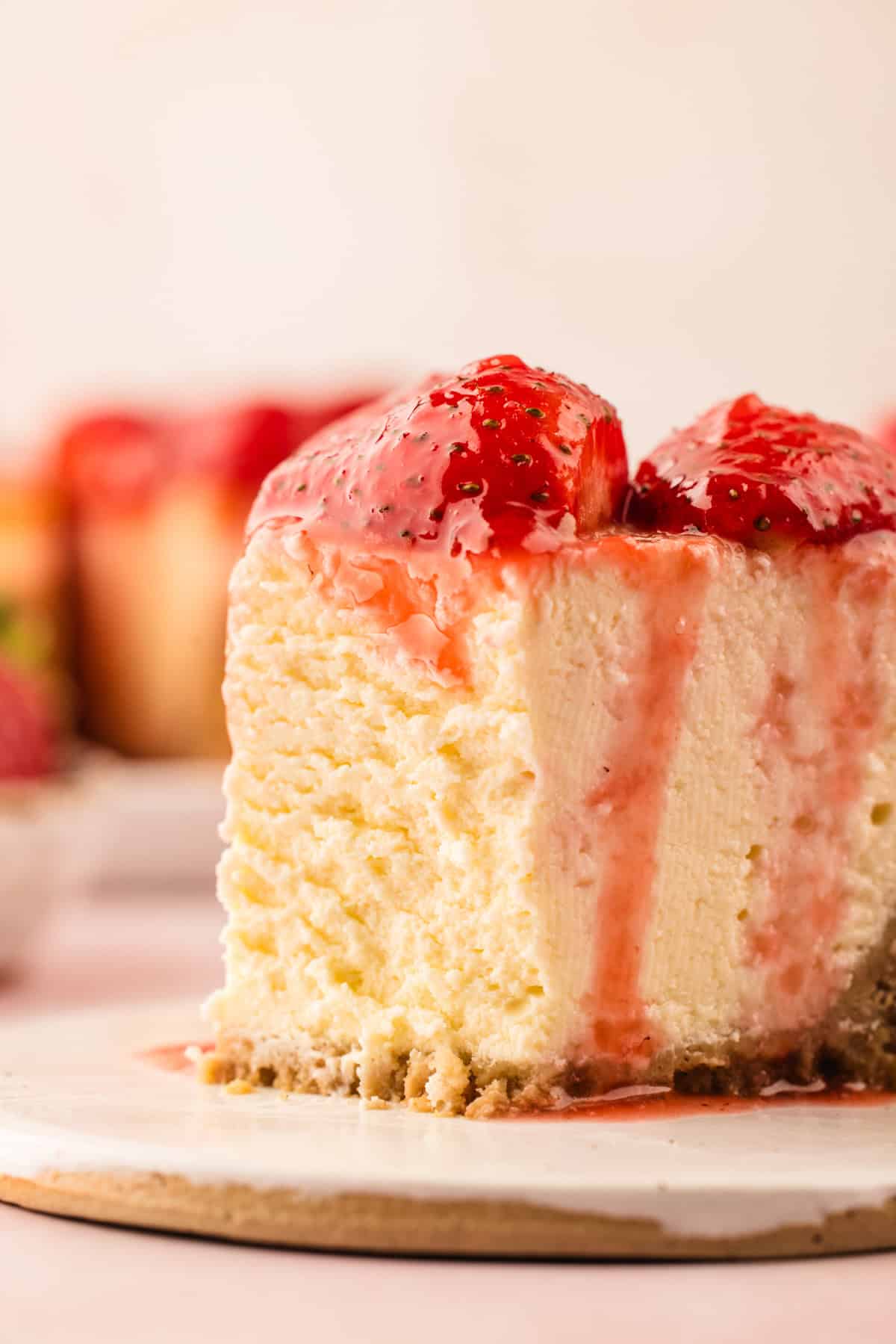Classic New York-Style Cheesecake A close-up of a slice of cheesecake topped with glossy strawberry sauce.