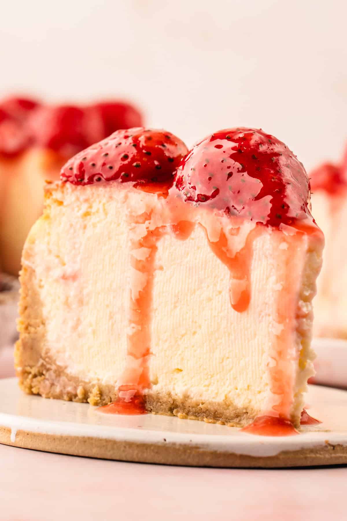 Classic New York-Style Cheesecake A slice of creamy cheesecake with a graham cracker crust, topped with fresh strawberries and dripping strawberry sauce.