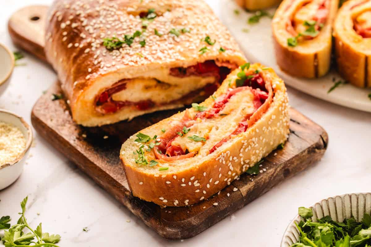 Stromboli A sliced loaf of stromboli filled with cheese and meat sits on a wooden board, topped with sesame seeds and chopped parsley.