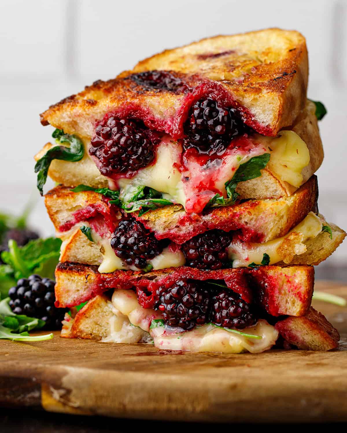 Stacked grilled cheese sandwiches with melted cheese, greens, and juicy blackberries.