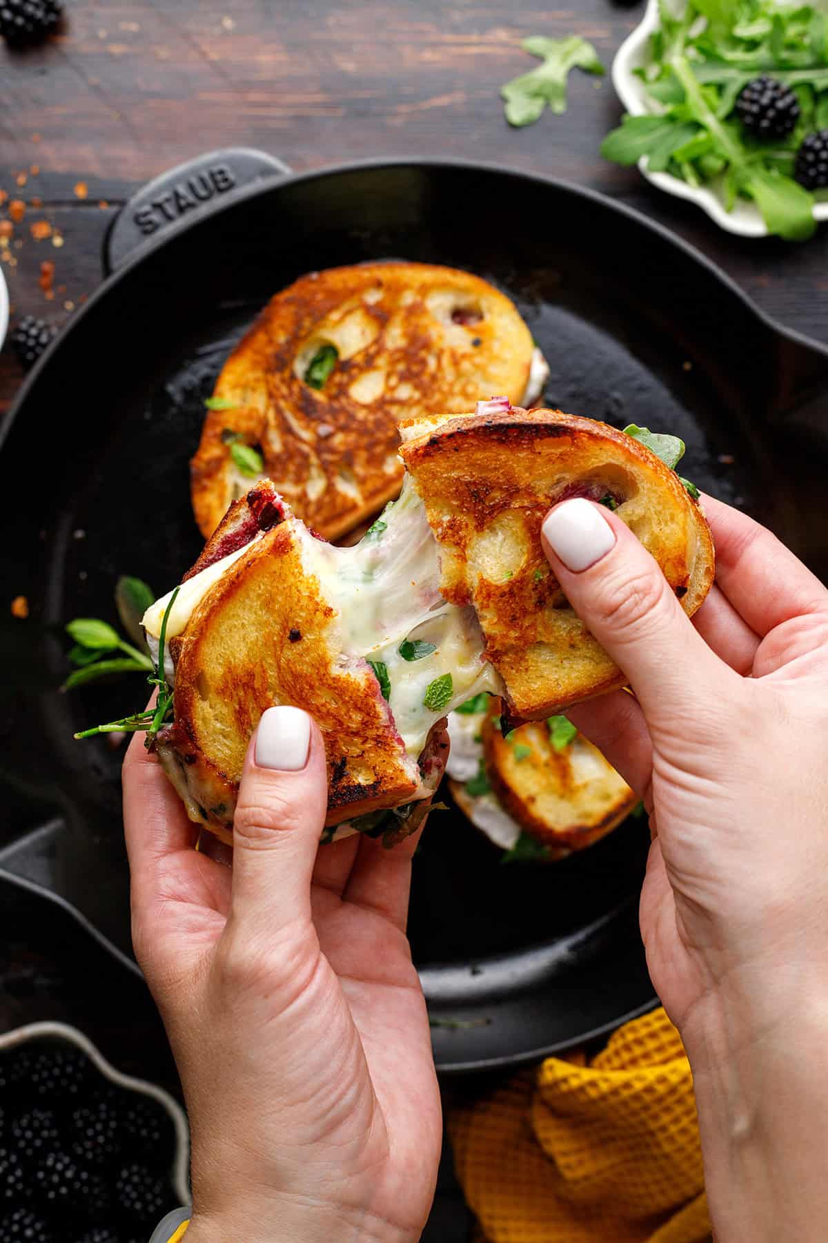Two hands pull apart a grilled cheese sandwich, showing melted cheese stretching between slices.