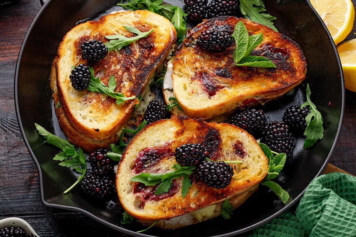 Three grilled sandwiches with melted cheese, blackberries, and greens.