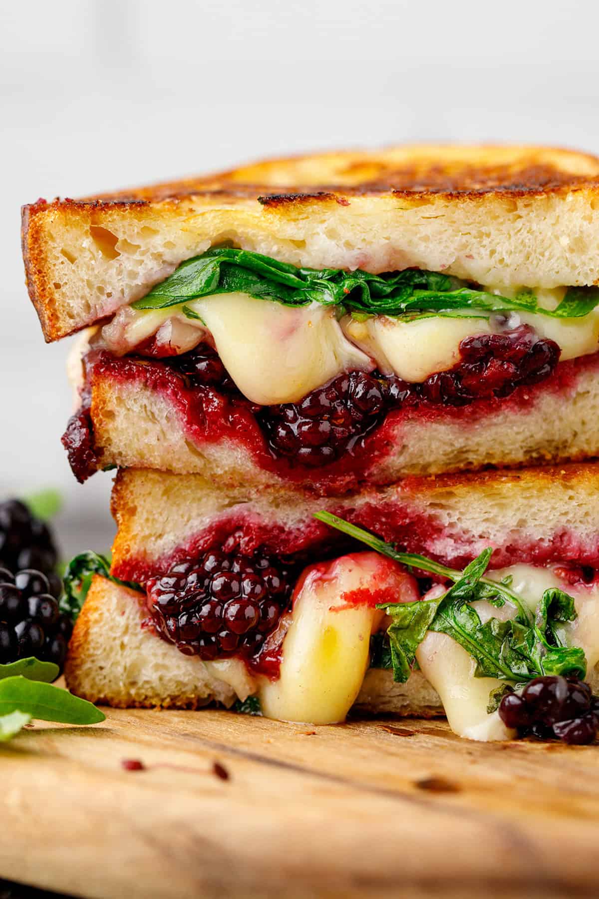 A grilled cheese sandwich stacked in halves, filled with melted cheese, fresh greens, blackberries, and berry jam.
