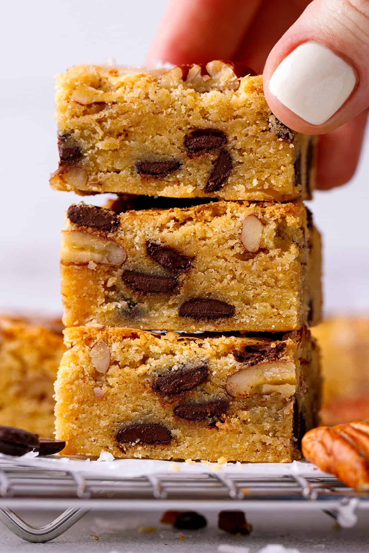 Blondies A hand picks up a blondie with chocolate chips and nuts from a stack of three.