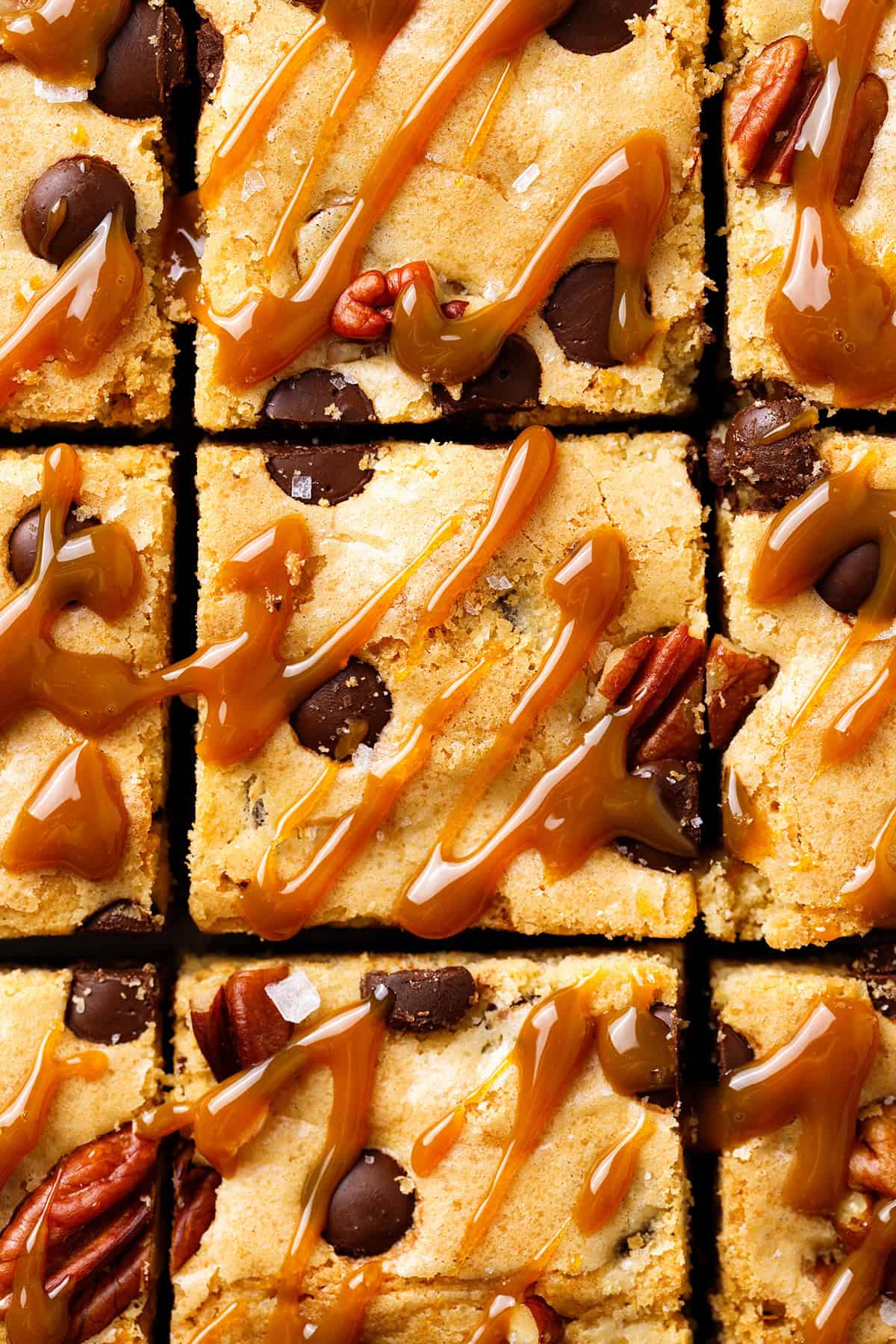 Blondies Close-up of blondie bars topped with caramel drizzle, pecans, and chocolate chips, cut into neat squares.