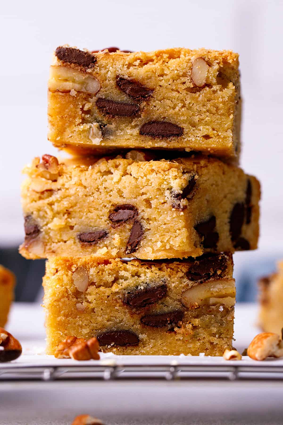 Blondies Three thick blondie bars with chocolate chips and nuts are stacked on top of each other on a cooling rack.