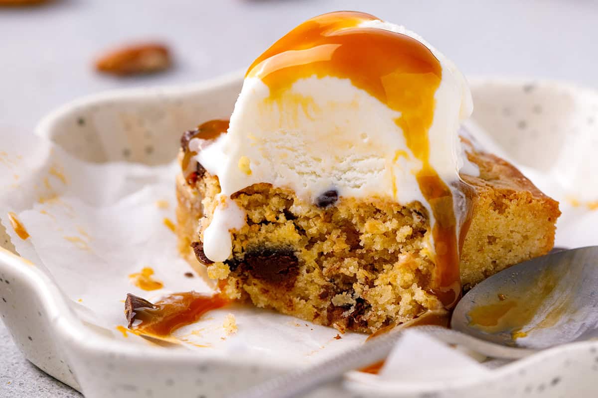 A blondie bar with a scoop of vanilla ice cream on a blondie, drizzled with caramel sauce.