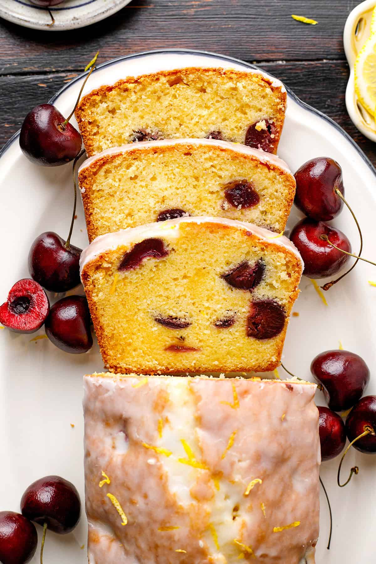 A sliced loaf cake with whole cherries inside is displayed on a white plate.