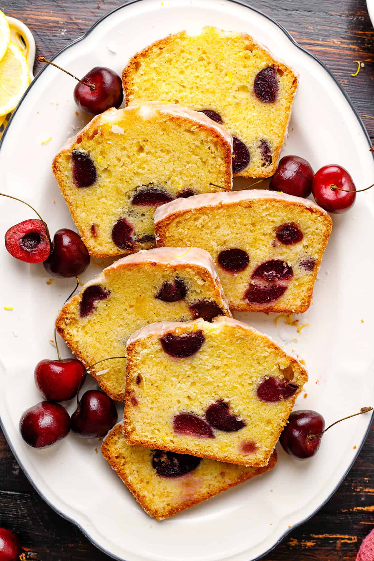 Cherry Loaf Cake Slices of cherry loaf cake with whole cherries scattered on a white oval plate.