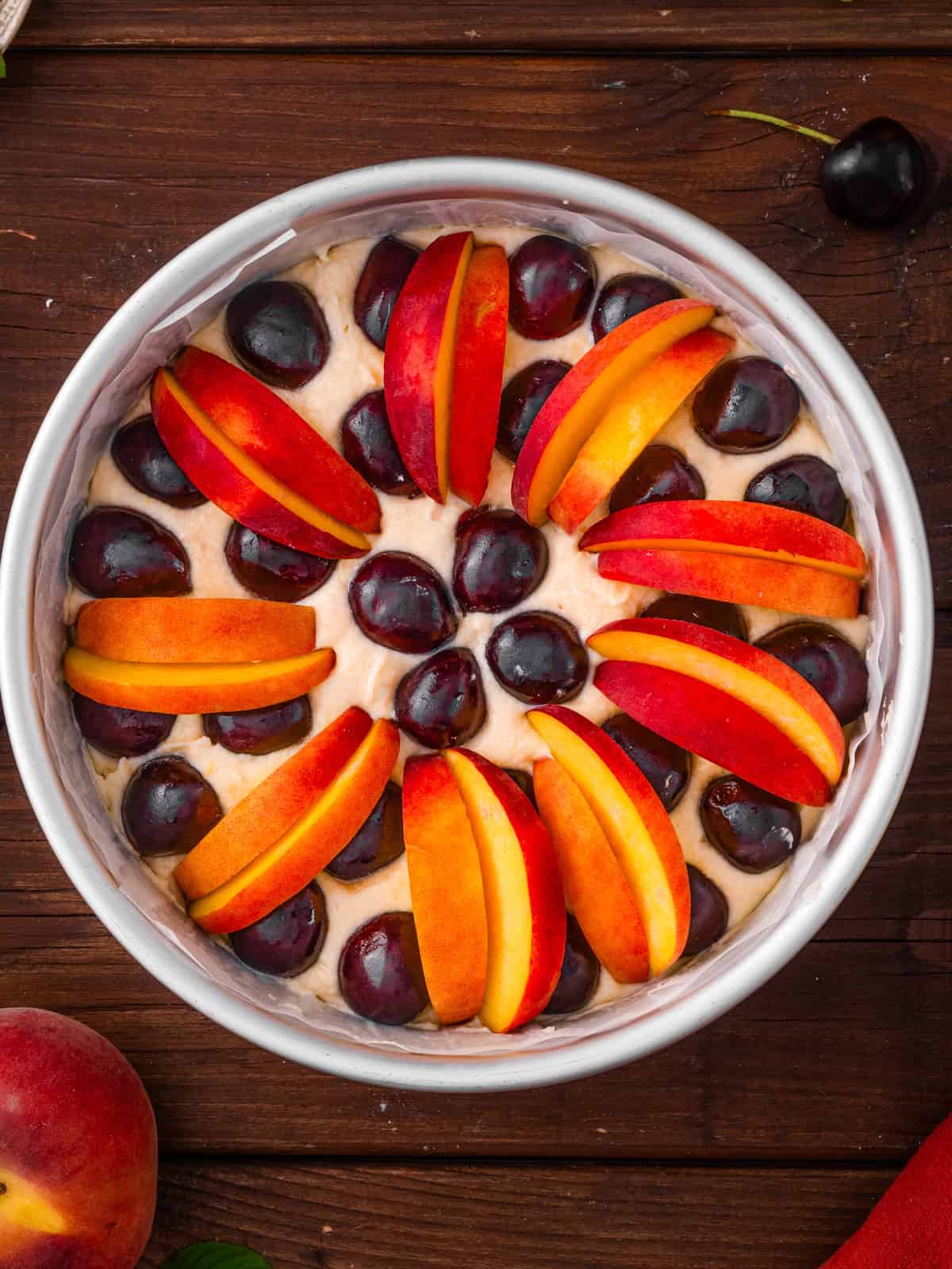 Italian-Style Lemon Ricotta Cake with Cherries and Peaches A round cake topped with alternating slices of peaches and whole cherries arranged in a circular pattern.