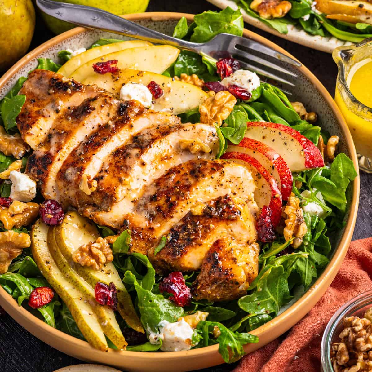 Chicken Arugula Salad with Pears, Goat Cheese, and Walnuts A bowl of salad with grilled chicken slices, mixed greens, apple and pear slices, walnuts, cranberries, and goat cheese.