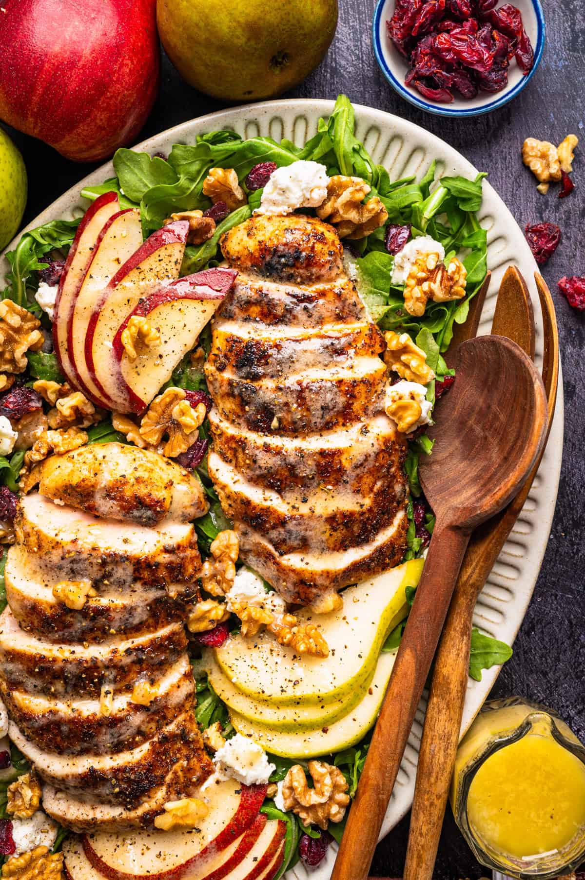 Chicken Arugula Salad A salad with sliced grilled chicken, apple and pear slices, walnuts, dried cranberries, cheese crumbles, and greens on a platter.