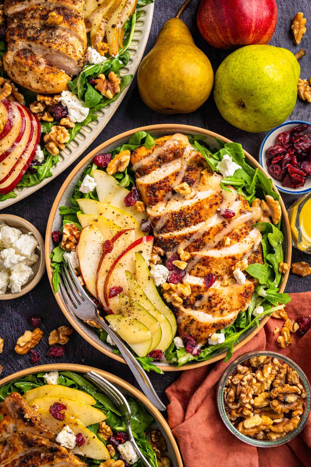 Chicken Arugula Salad A salad bowl with sliced grilled chicken, pear, apple, walnuts, mixed greens, and dried cranberries.
