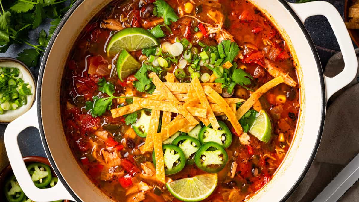 Chicken Tortilla Soup A pot of chicken tortilla soup topped with tortilla strips, sliced jalapeños, lime wedges, green onions, and cilantro.