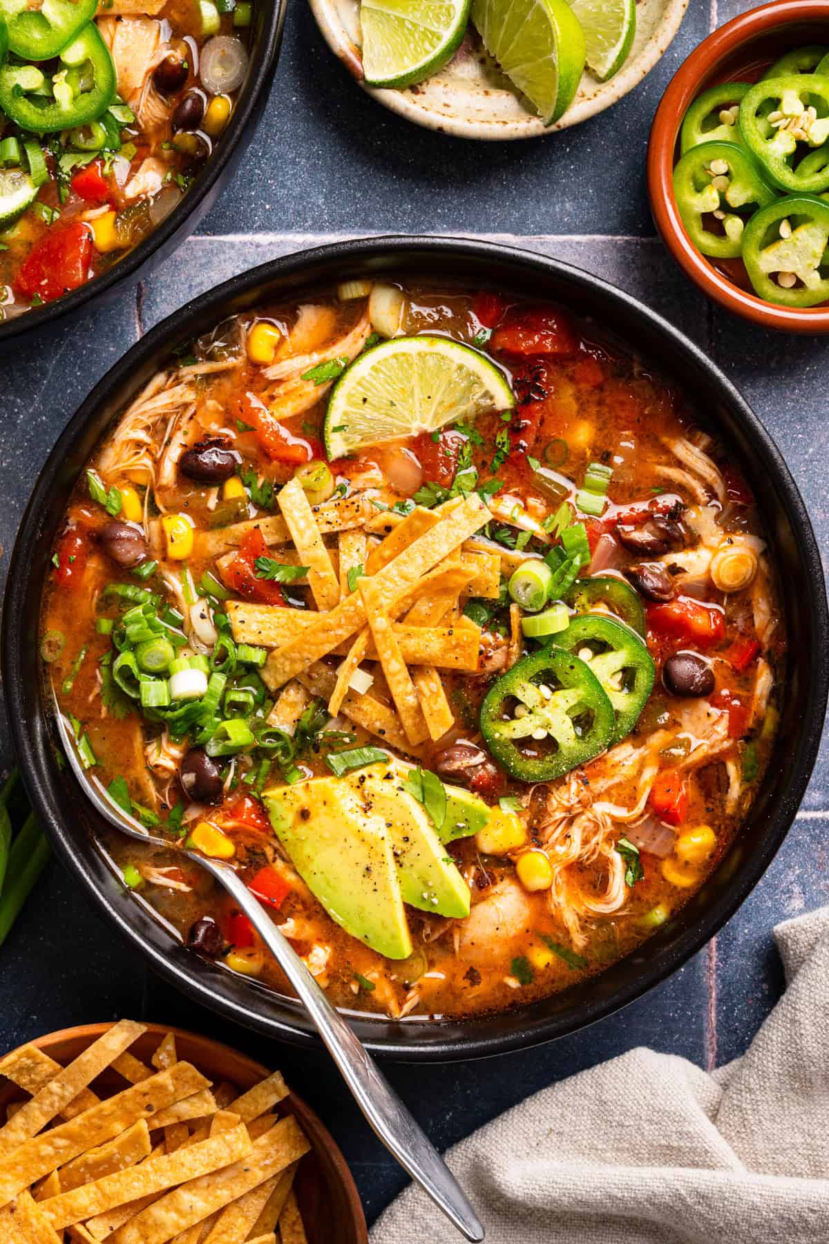 Chicken Tortilla Soup A bowl of chicken tortilla soup topped with avocado slices, tortilla strips, jalapeño, lime, green onions, and cilantro.