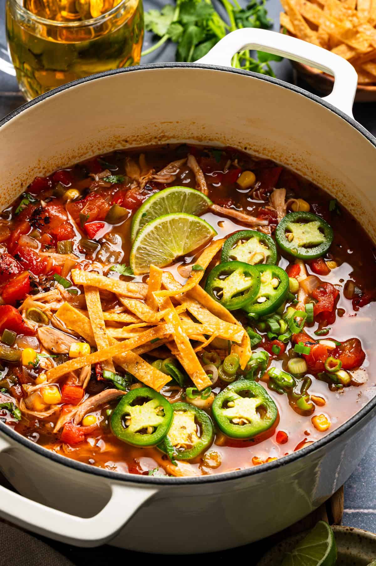 Chicken Tortilla Soup A pot of tortilla soup topped with lime slices, tortilla strips, and jalapeño rings, with visible vegetables and chicken in a flavorful broth.