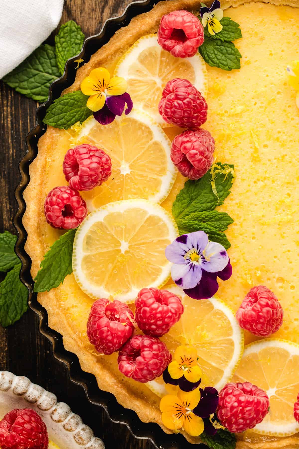Lemon Tart A lemon tart garnished with fresh raspberries, lemon slices, mint leaves, and edible flowers.