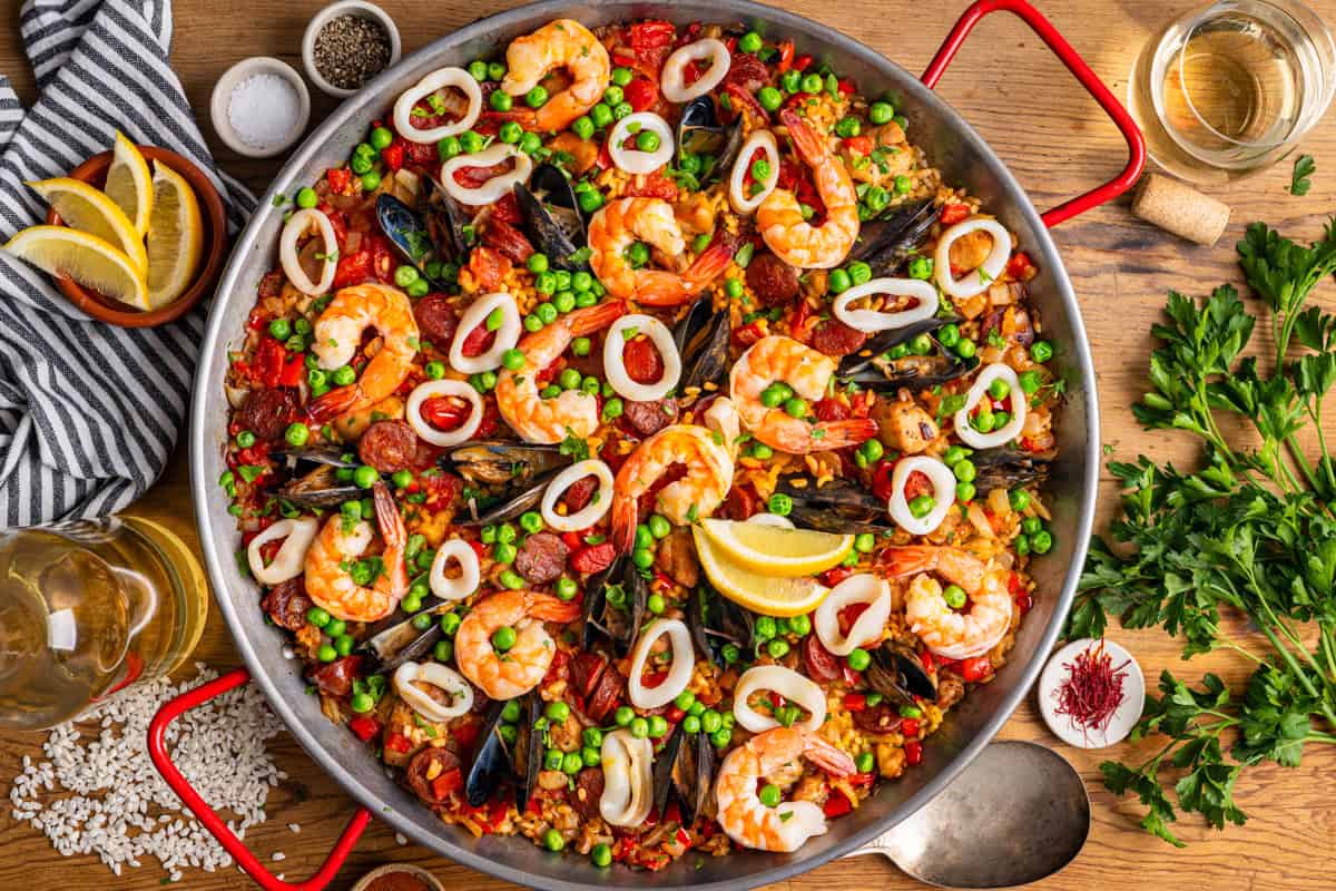 Paella A large pan of seafood paella with shrimp, mussels, squid rings, peas, red peppers, and lemon wedges on top.
