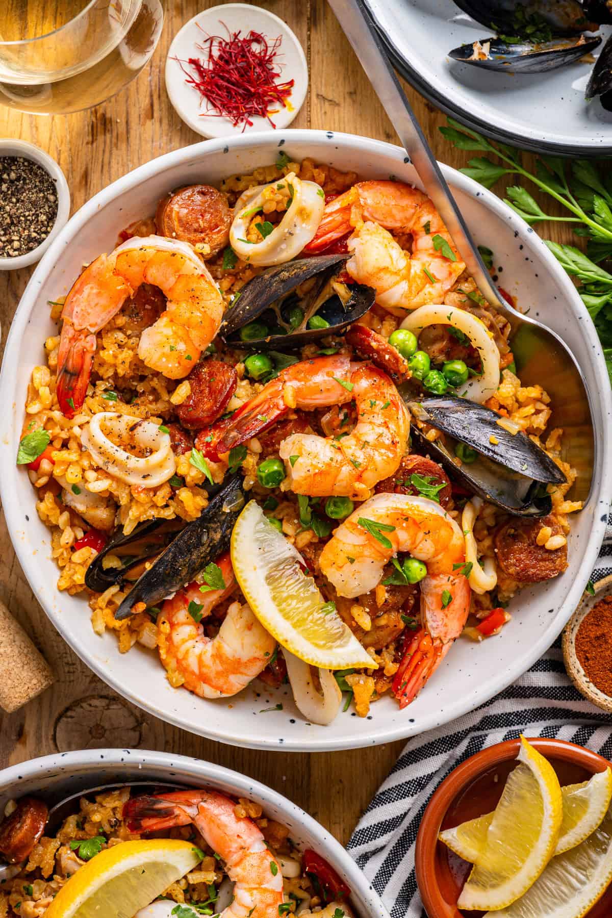 Paella A bowl of seafood paella topped with shrimp, mussels, calamari, peas, sausage, and lemon wedges.