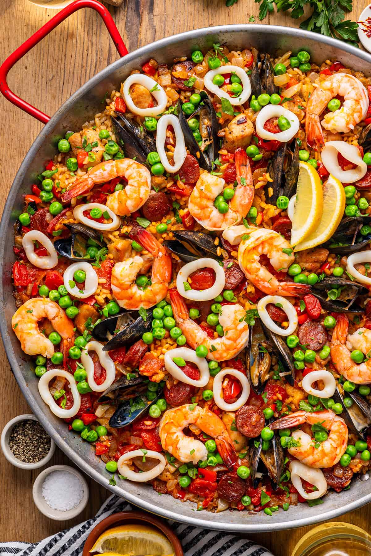 Paella A colorful seafood paella in a large pan with shrimp, mussels, squid rings, peas, lemon wedges, chorizo, and rice.