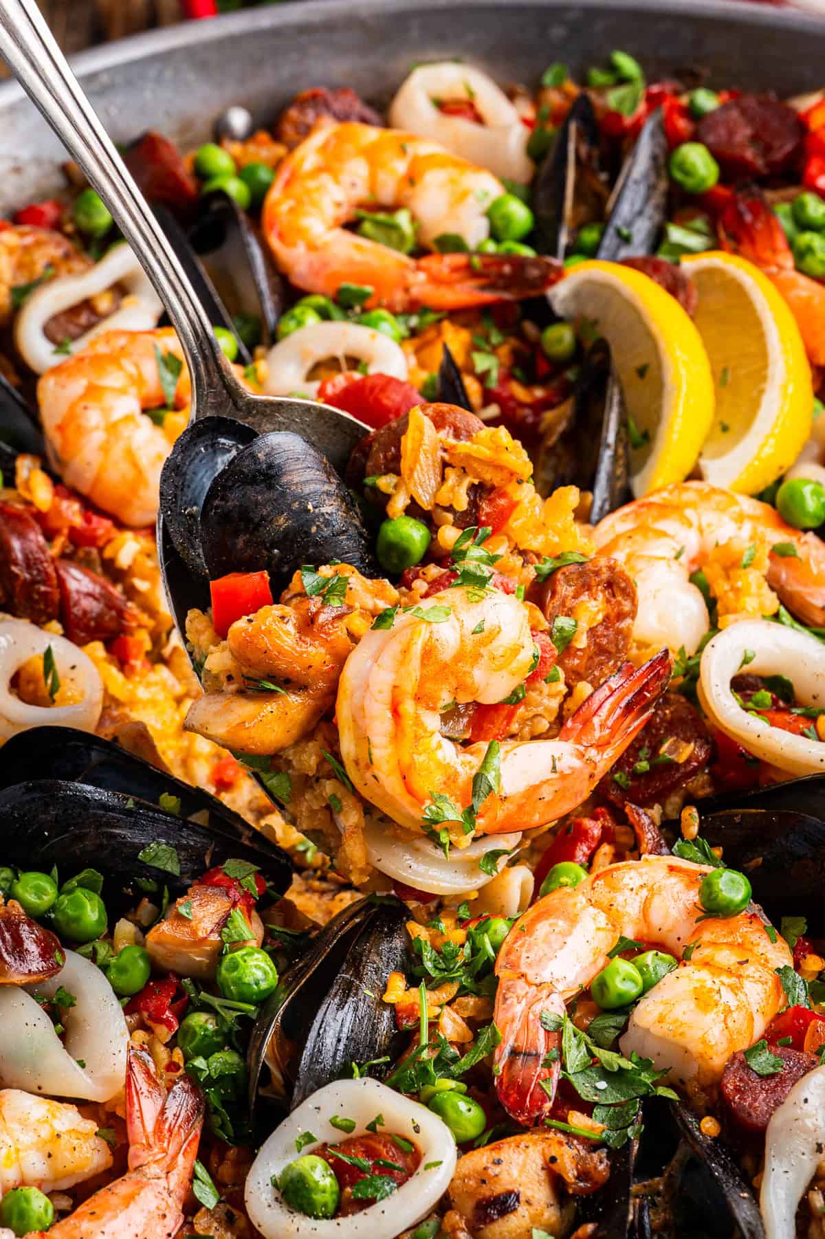 Paella Close-up of colorful seafood paella with shrimp, mussels, squid, peas, and lemon slices.